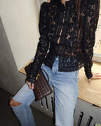 A woman wearing a black Fontaine lace blouse by WOLZI and light blue jeans.
