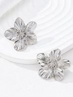 WOLZI silver-toned textured flower stud earrings on a white plate