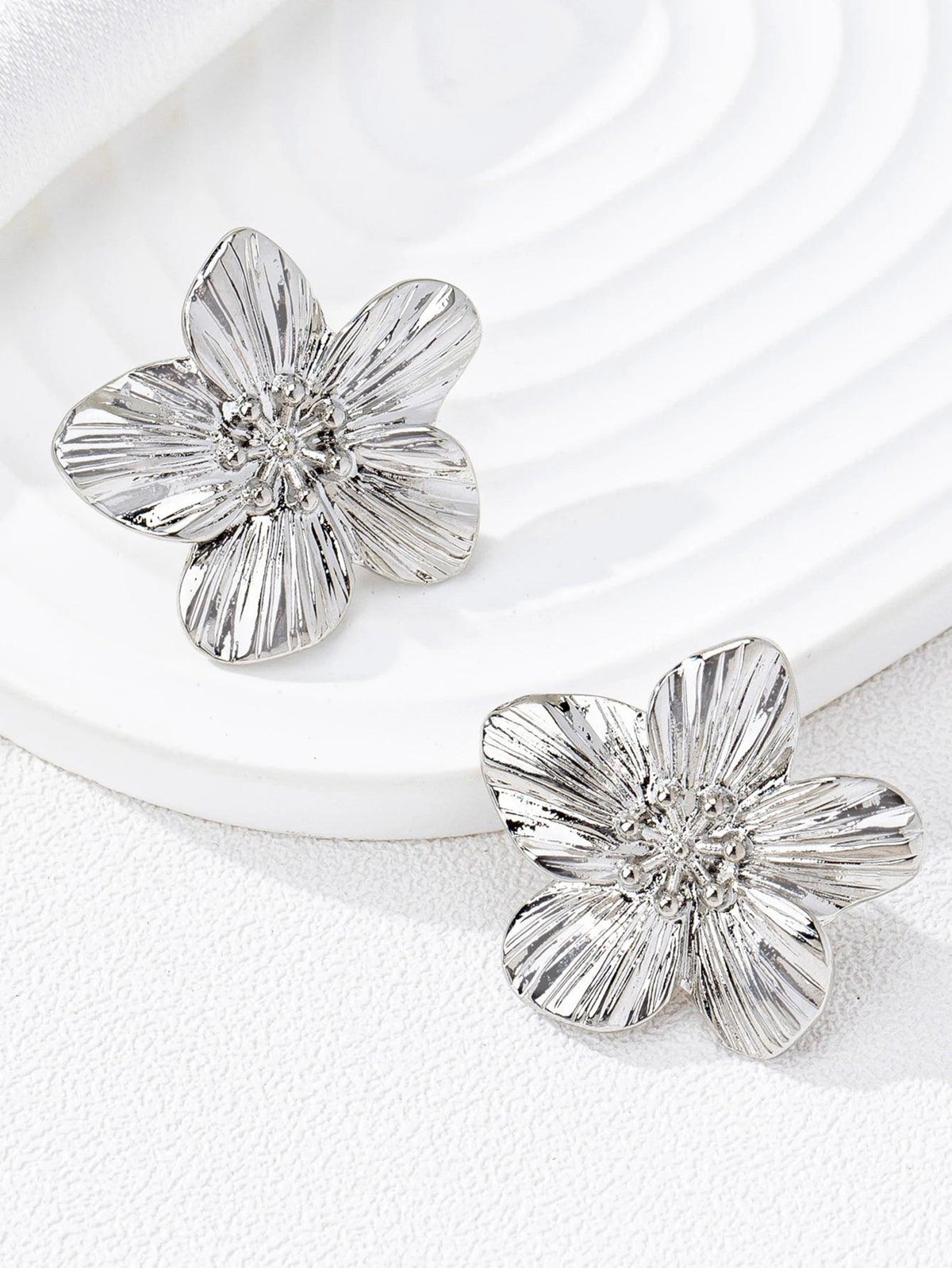 WOLZI silver-toned textured flower stud earrings on a white plate