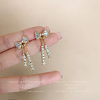 WOLZI Elodie Crystal Bow Stud Earrings with dangling rhinestone tassels held in hand