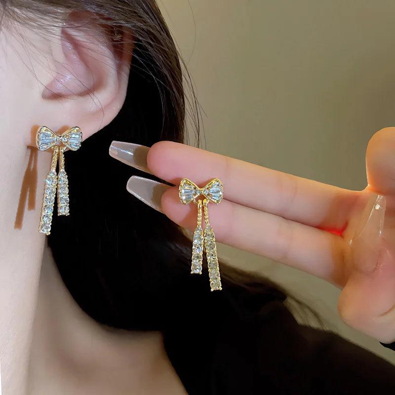 WOLZI Elodie Crystal Bow Stud Earrings in gold tone with dangling stones.