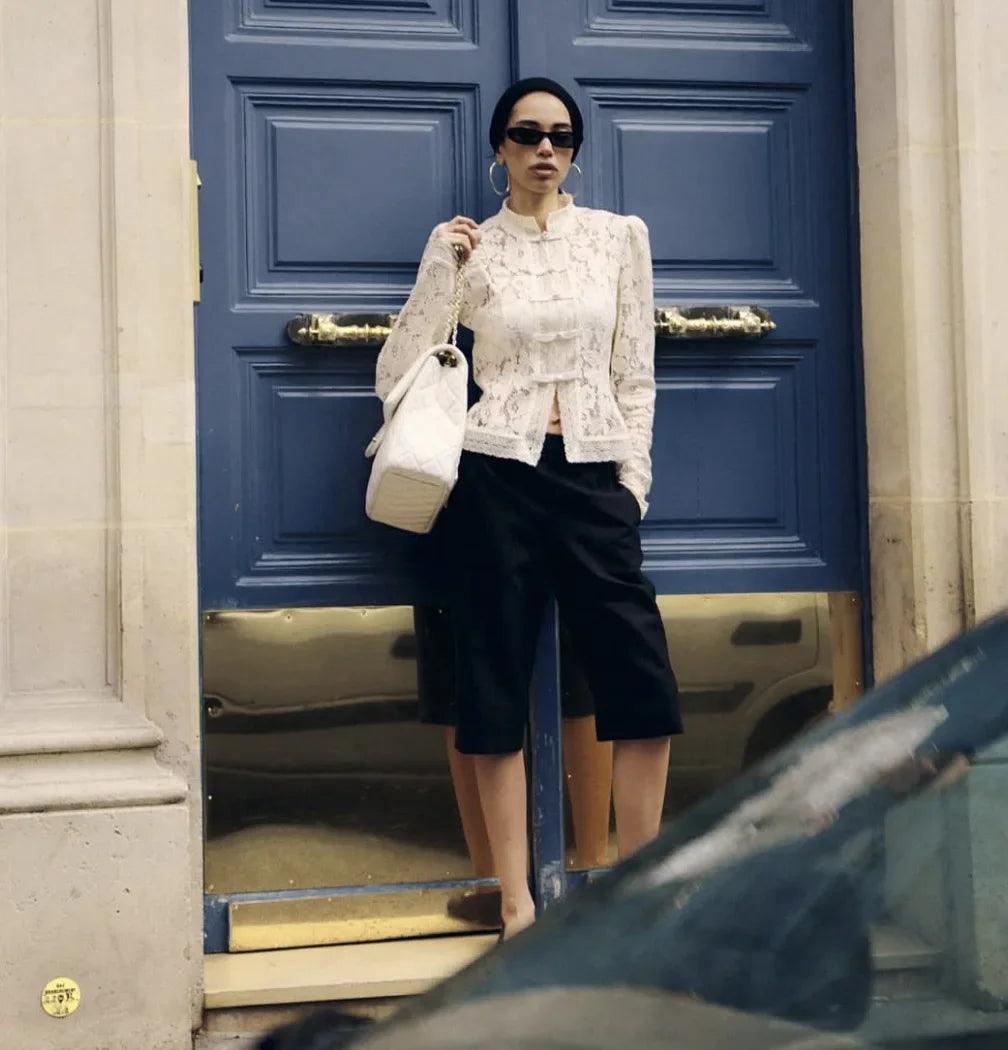 Woman wearing WOLZI Fontaine Lace Blouse in beige with black shorts and a white handbag.