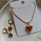 WOLZI Amoura rose gold heart jewelry set featuring a necklace and matching hoop earrings.
