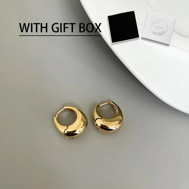 WOLZI Aurelle Sculpted Oval Gold Hoop Earrings with gift box on a white plate.