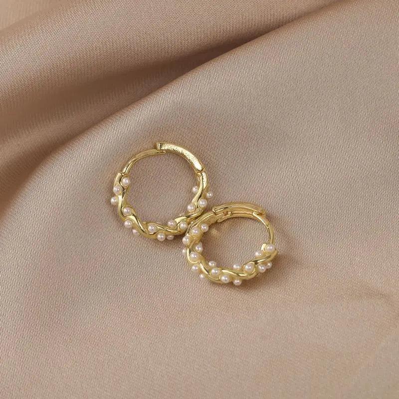 WOLZI Lumi Pearl Circle Stud Earrings in gold with delicate pearl accents on beige fabric.